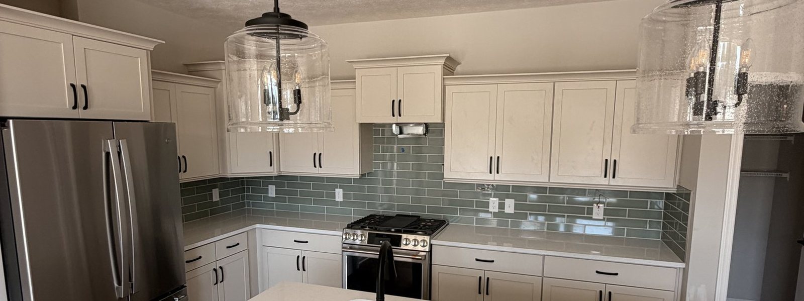 White kitchen island with sink and pendant lighting beneath a glass tile backsplash