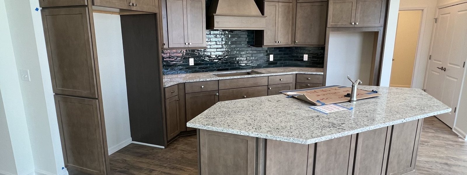 Finished kitchen with stained cabinetry, granite island and tile backsplash