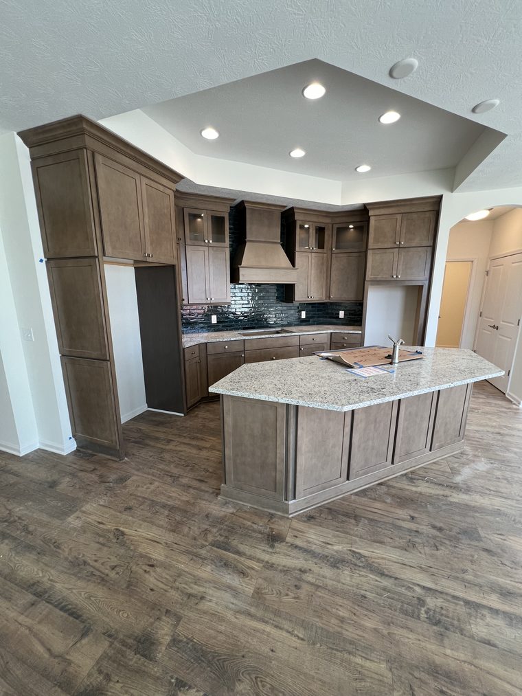 Finished kitchen with stained cabinetry, granite island, vented hood and dark tile backsplash