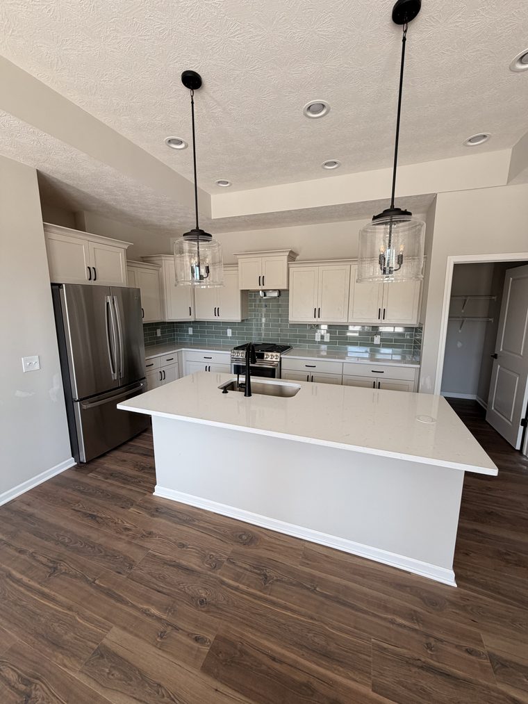 Finished kitchen with white cabinetry, a waterfall island, glass tile backsplash and pendant lighting