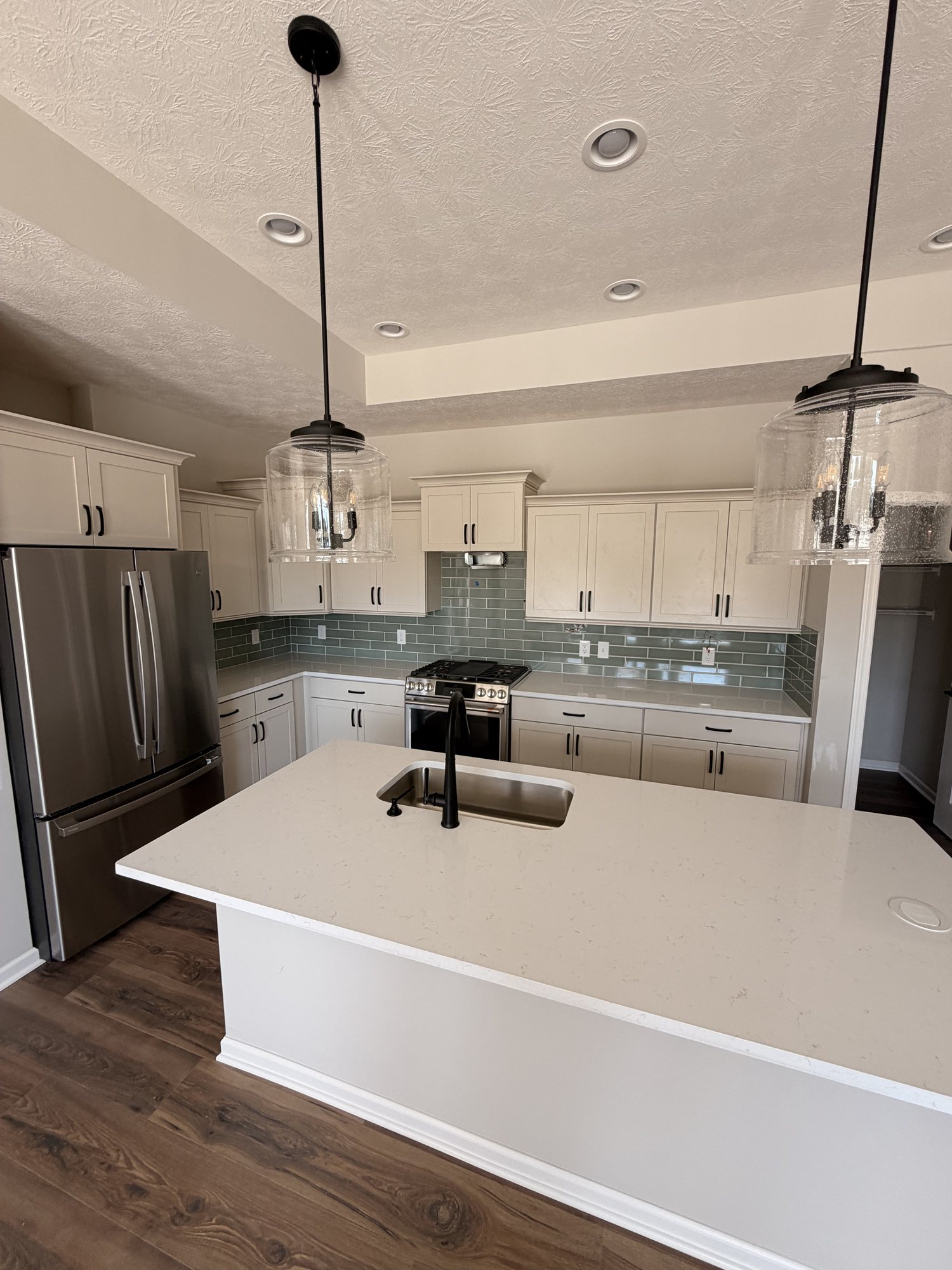White kitchen island with sink and pendant lighting, seen from the range wall