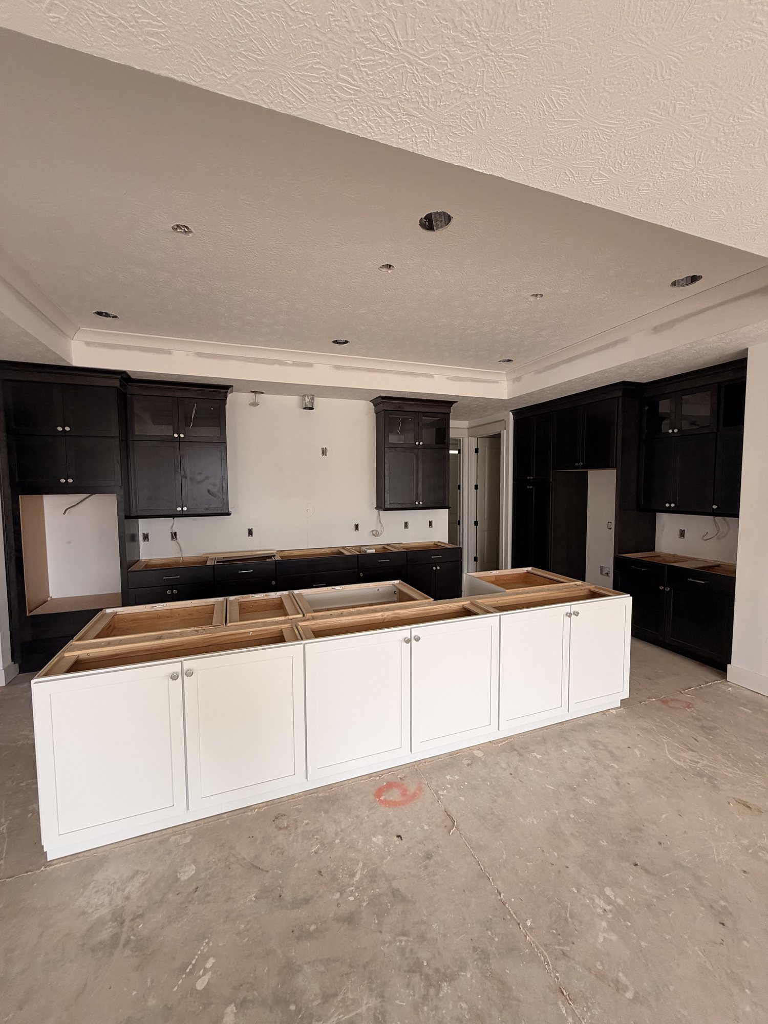 Dark perimeter cabinetry with a white island set, before tops