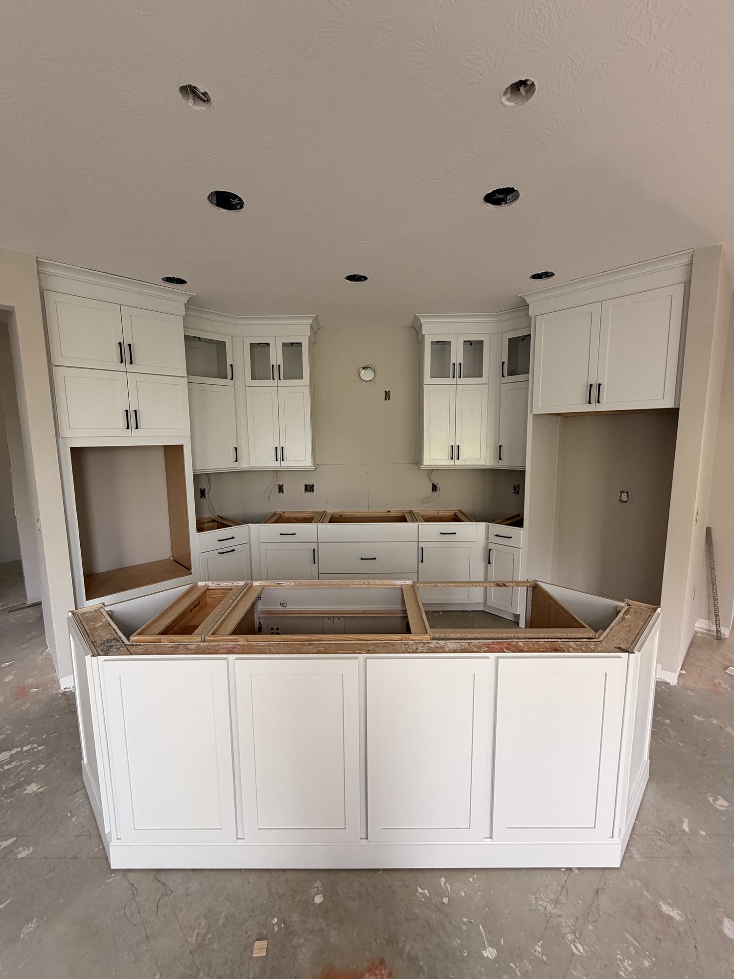 White kitchen cabinetry and island set, waiting on countertops