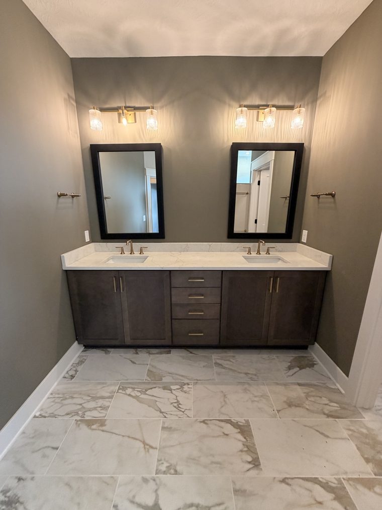 Finished bathroom with a dark double vanity, twin mirrors and marble-look tile floor