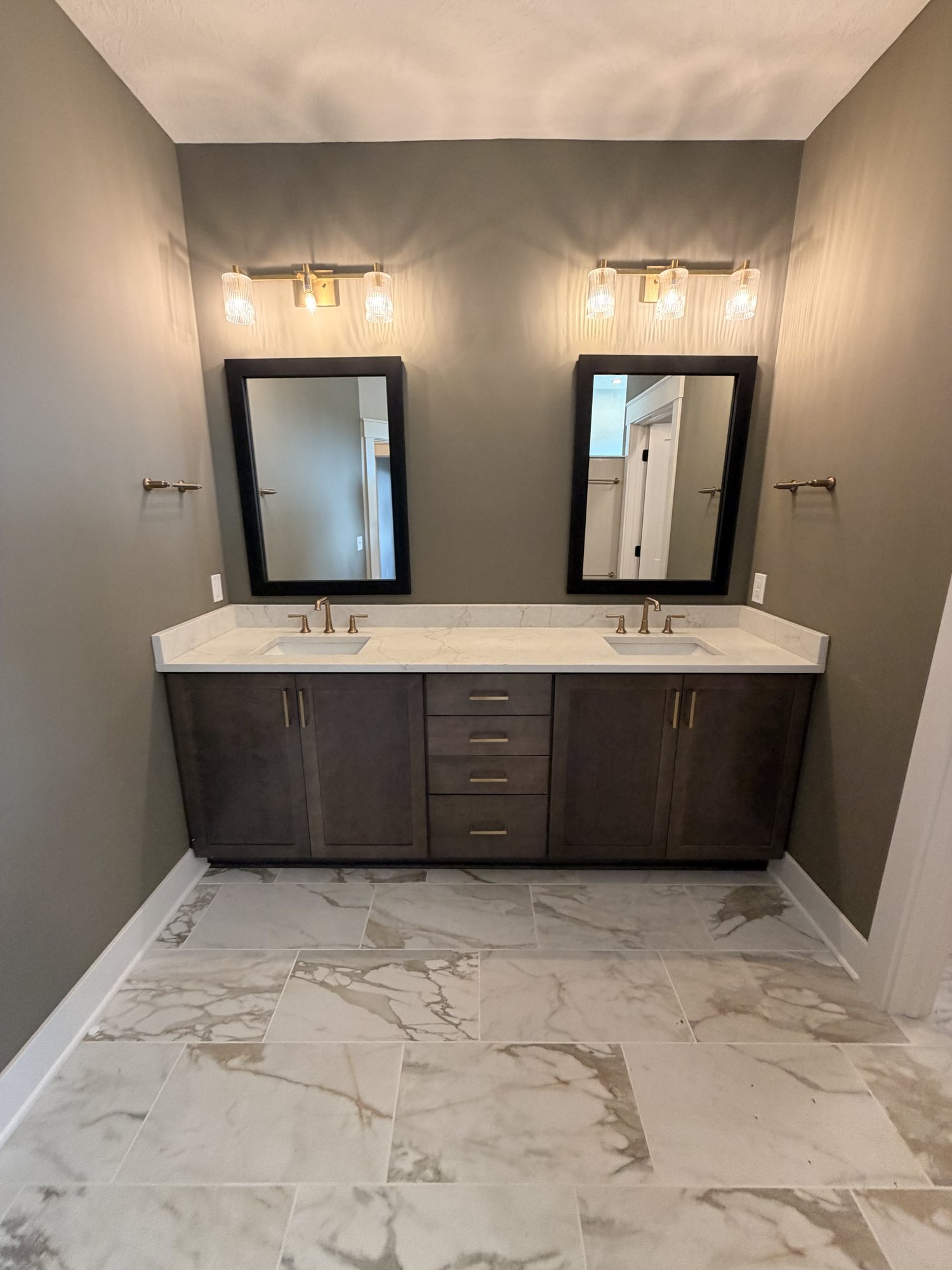 Finished bathroom with a dark double vanity, twin mirrors and marble-look tile floor