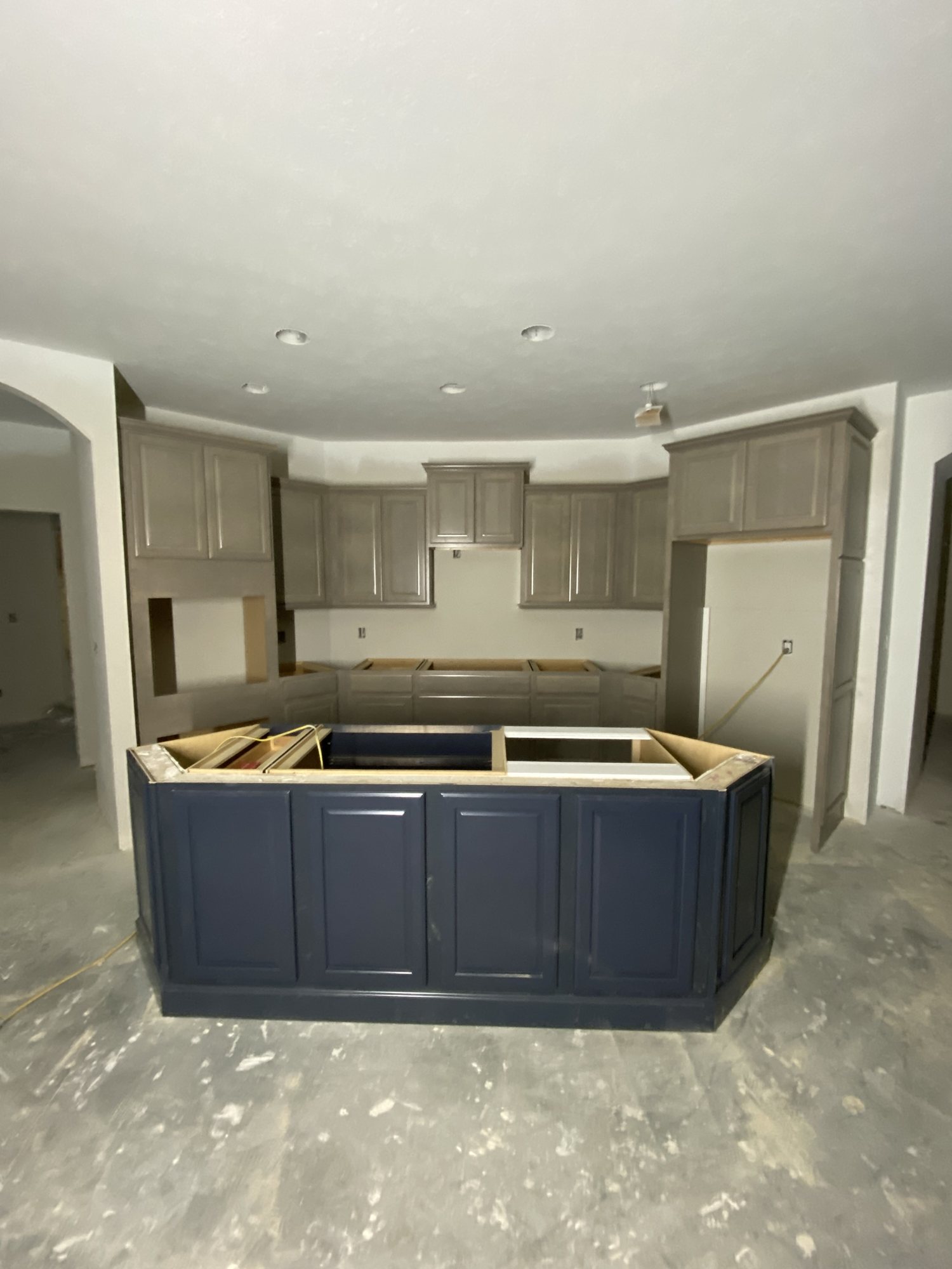 Kitchen with stained perimeter cabinetry and a navy island, mid-install