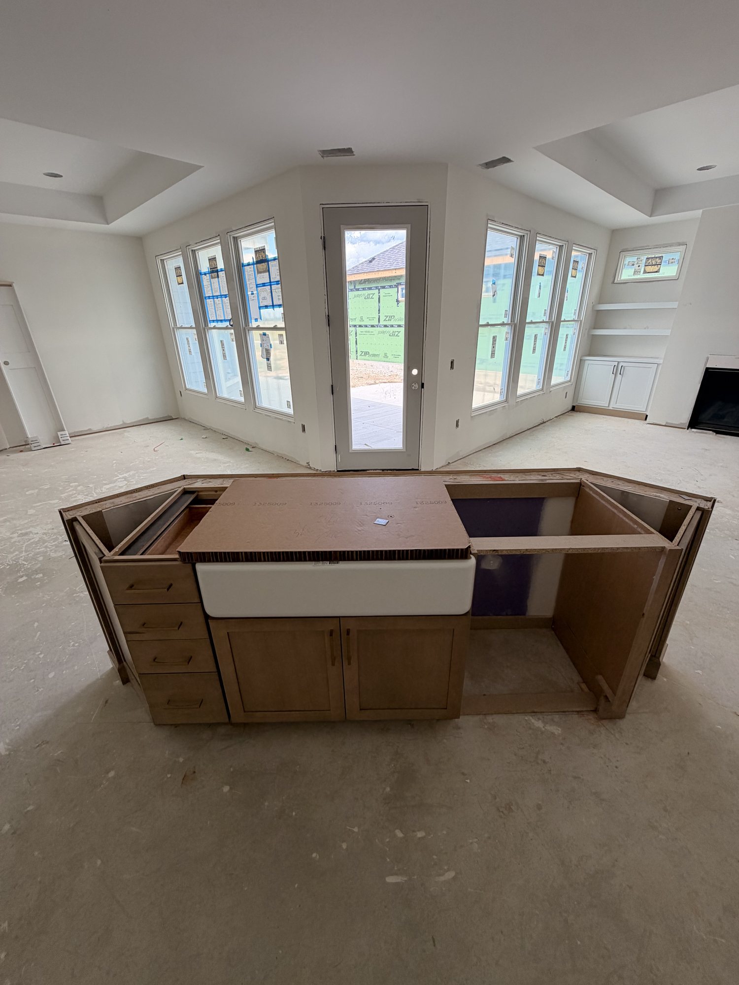 Large kitchen island with farmhouse sink set under bay windows, before countertops